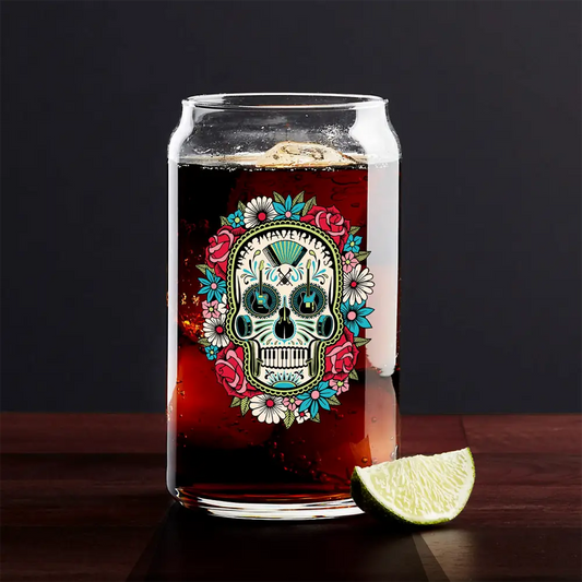 Glass of dark beverage with a colorful sugar skull design on the side, accompanied by a lime wedge.