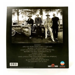 Back cover of a music album featuring a black and white photograph of four men posing next to a vintage car, with a track listing below.